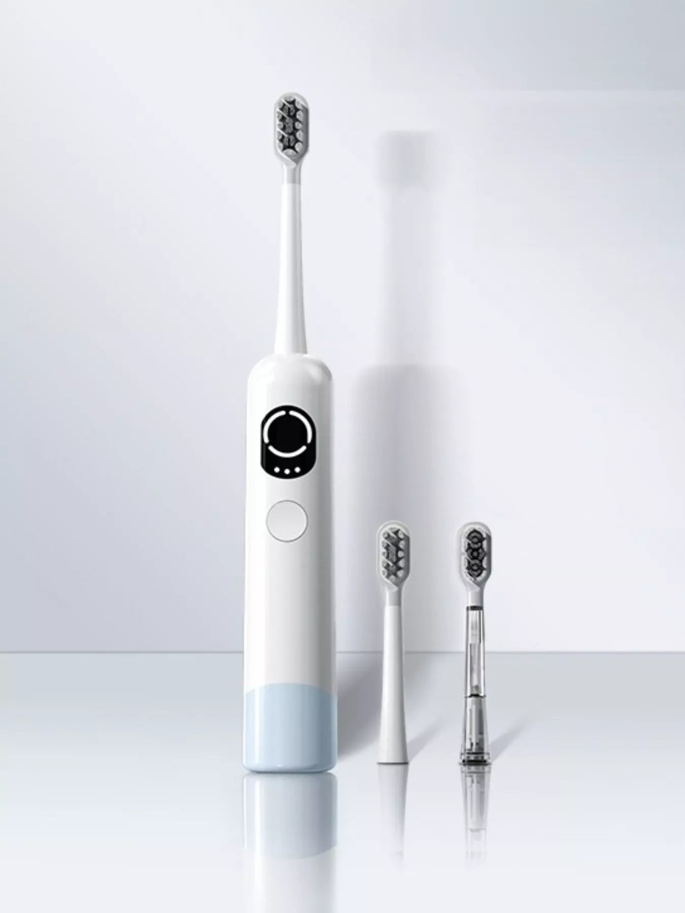 A white electric toothbrush with a display stands upright beside three interchangeable brush heads, one of which has a transparent base, against a minimal, light background.
