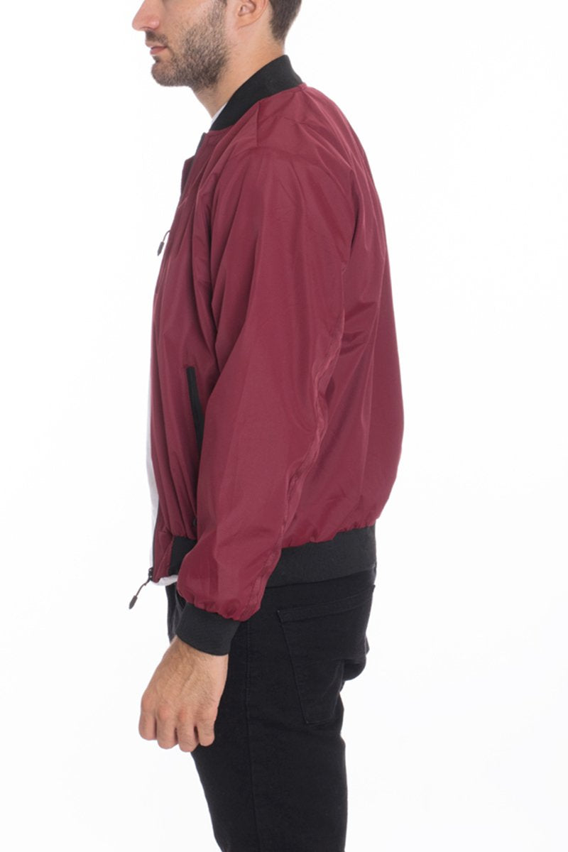 A man in profile models the Lime Milo Mens Vinyl Waterproof Windbreaker—a maroon, slim-fit jacket with black cuffs, collar, and waistband—paired with black pants against a plain white background.