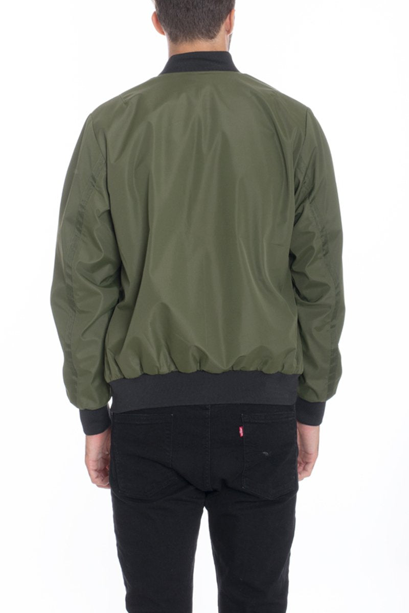 A person stands with their back to the camera, wearing the Lime Milo Mens Vinyl Waterproof Windbreaker in green and black jeans against a plain white background.