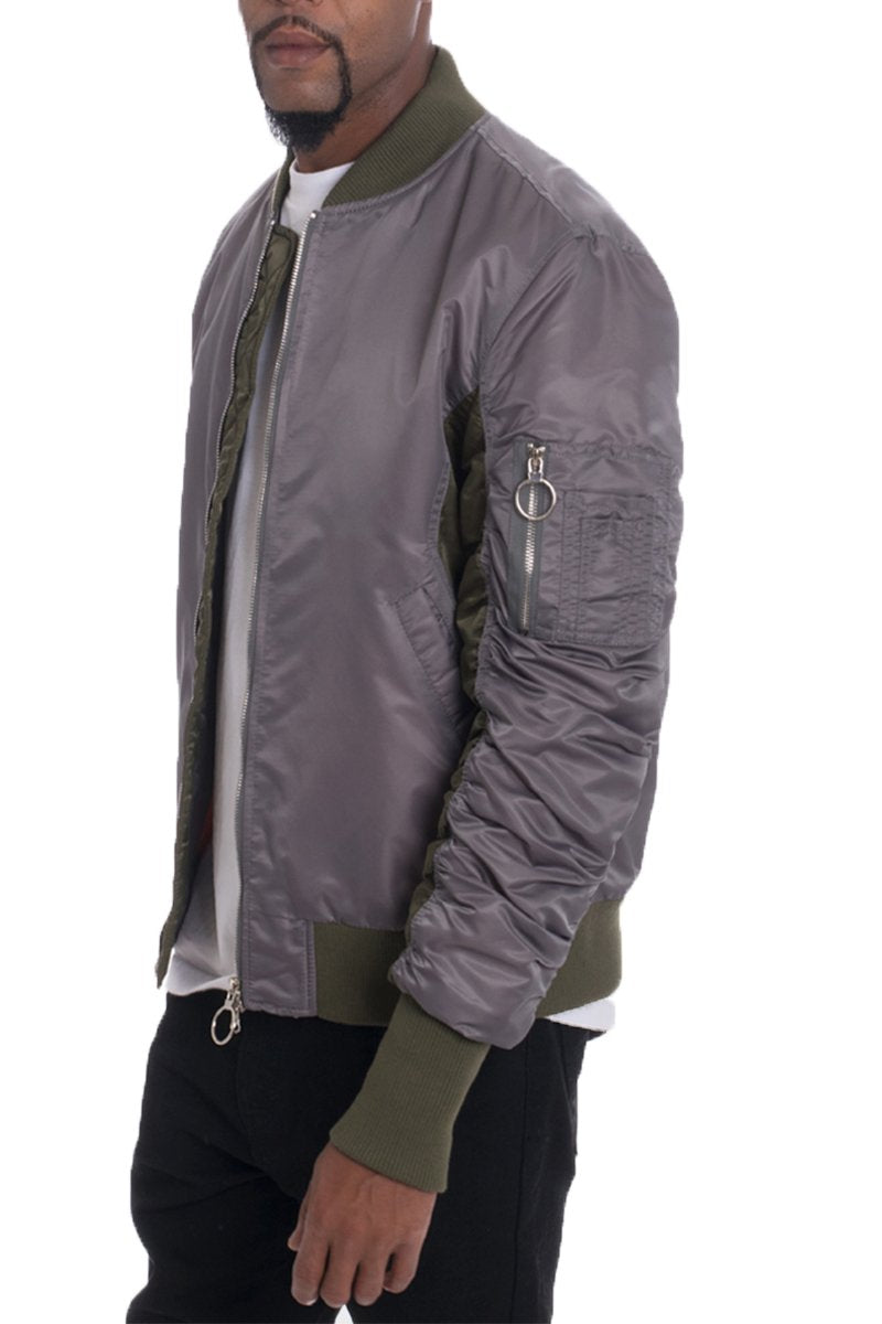 A man wears the Lime Milo TWO TONE BOMBER, featuring a shiny gray body with green cuffs and collar, over a white t-shirt and black pants, standing against a plain white background.