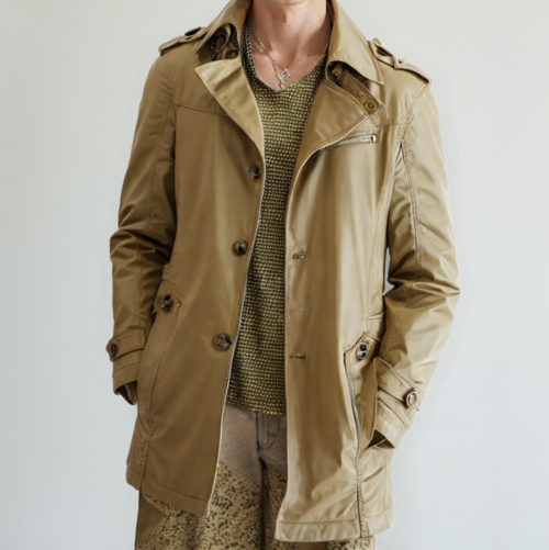 A man wears the Yellow Pandora Mens Classic Trench Coat in light brown over a green knit sweater and light brown patterned pants, standing with hands in coat pockets against a plain light background.
