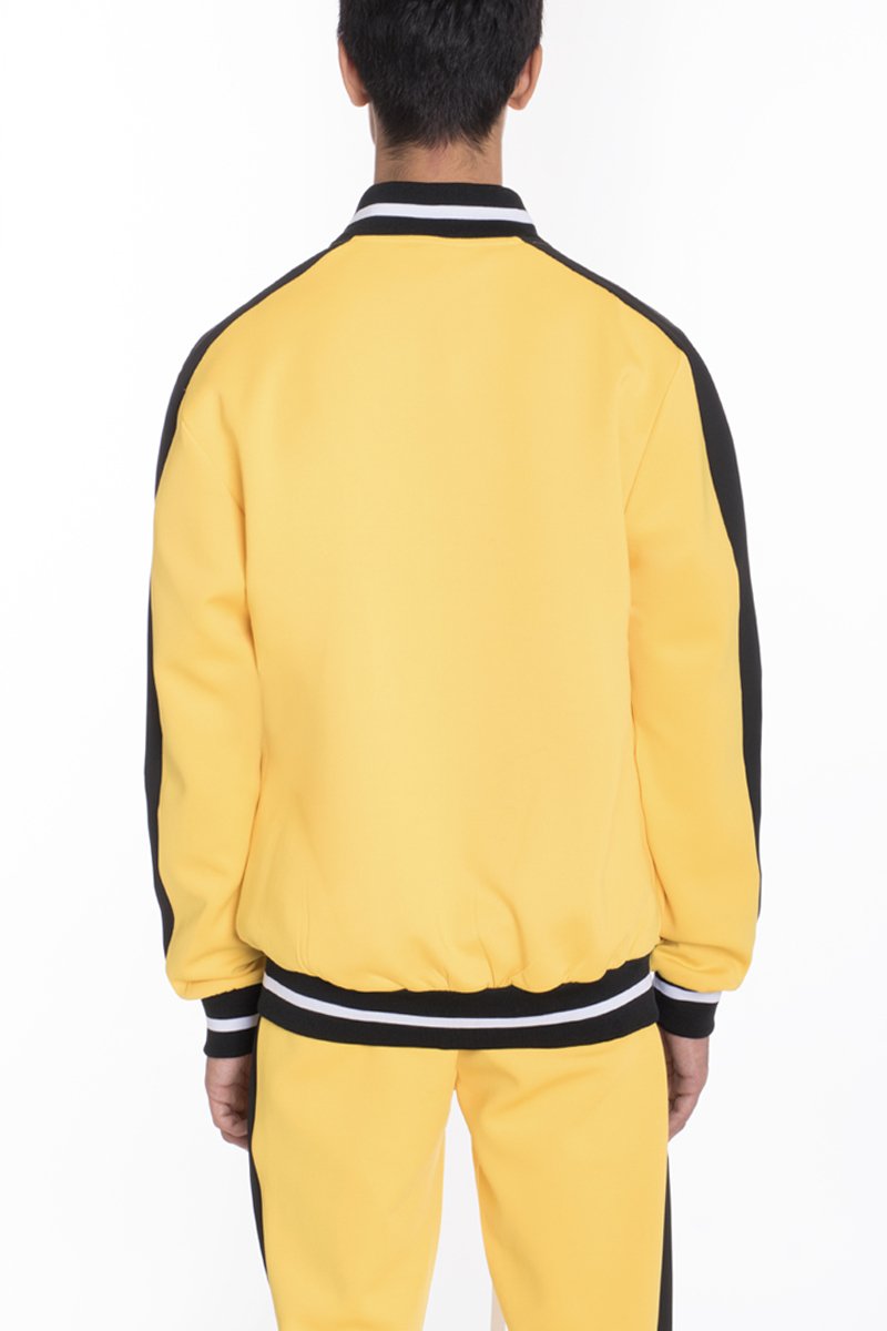 A person faces away from the camera, wearing Lime Milo's Heavy Weight Solid Track Jacket in yellow with matching pants, featuring black side stripes and black-and-white striped cuffs, collar, and waistband against a plain white background.