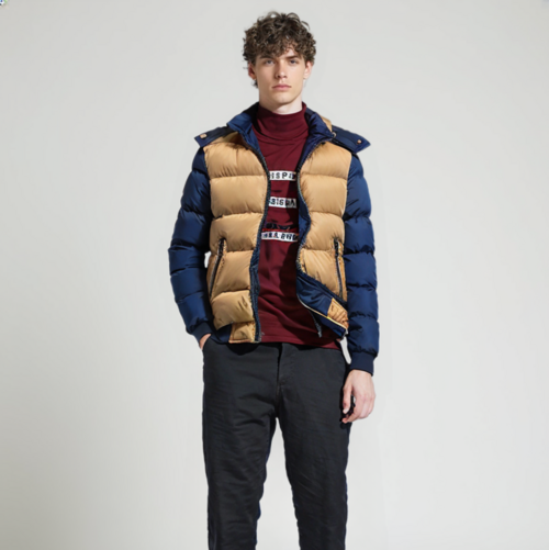 A young man with curly hair stands against a plain light background, wearing the Yellow Pandora Men's Two Tone Puffer Jacket with Removable Hood over a maroon turtleneck and black pants. His hands are relaxed by his sides.